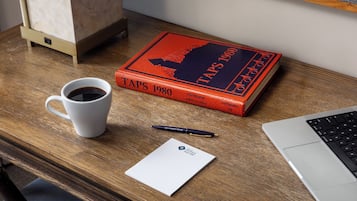 Un escritorio de madera con una computadora portátil, una taza de café, un bolígrafo, un cuaderno y un libro titulado