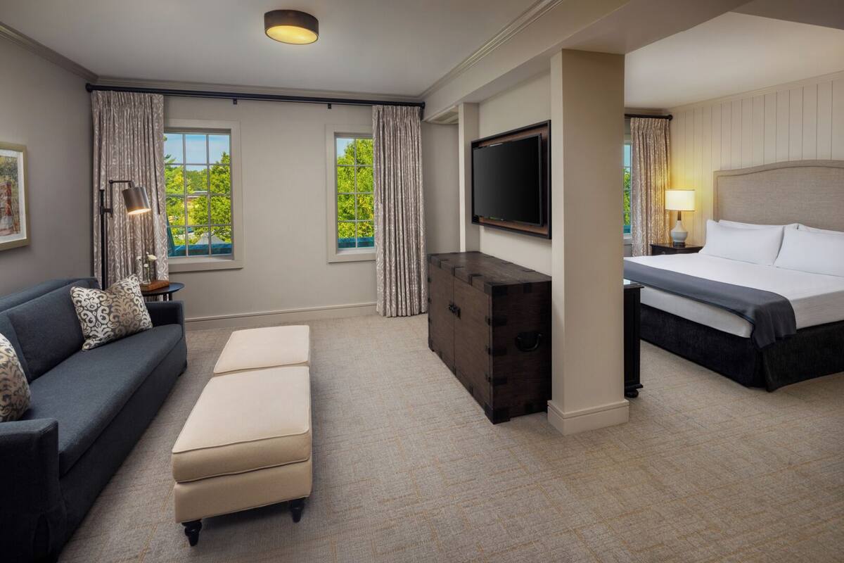 A hotel room with a bed, a sofa, a TV, a dresser, and a window with curtains.