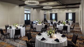 A banquet hall with round tables set for dining, featuring chandeliers and a carpeted floor.