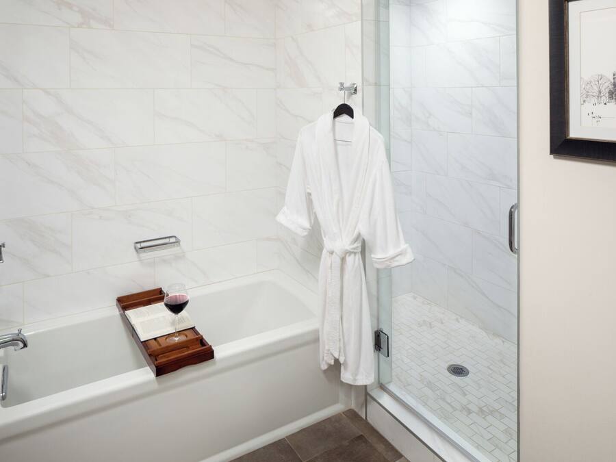 A modern bathroom with a marble wall, a bathtub, a glass-enclosed shower, and a framed picture on the wall.