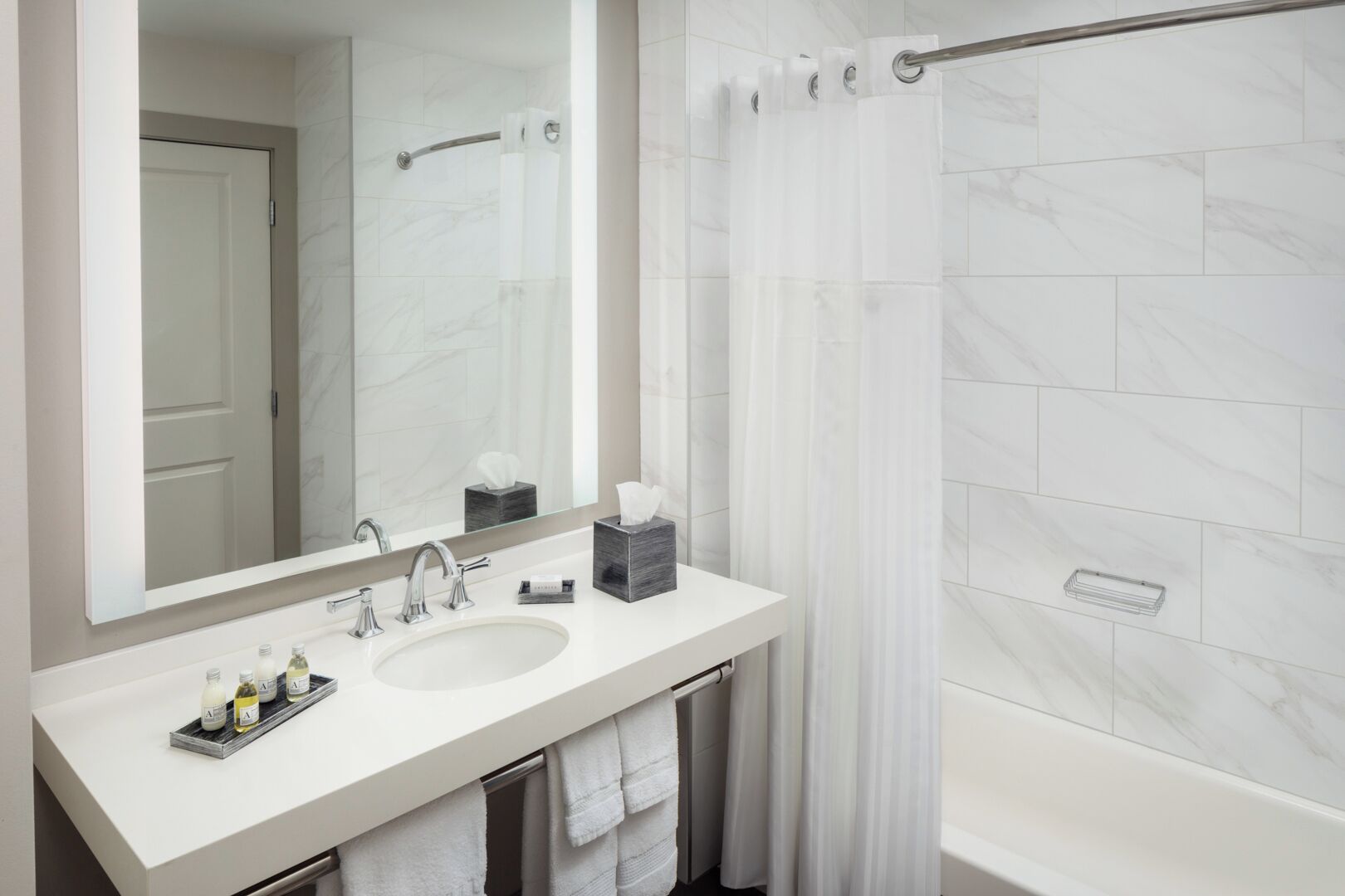 Un baño moderno con un espejo grande, dos lavamanos, una ducha con puerta de vidrio y un perchero para toallas.