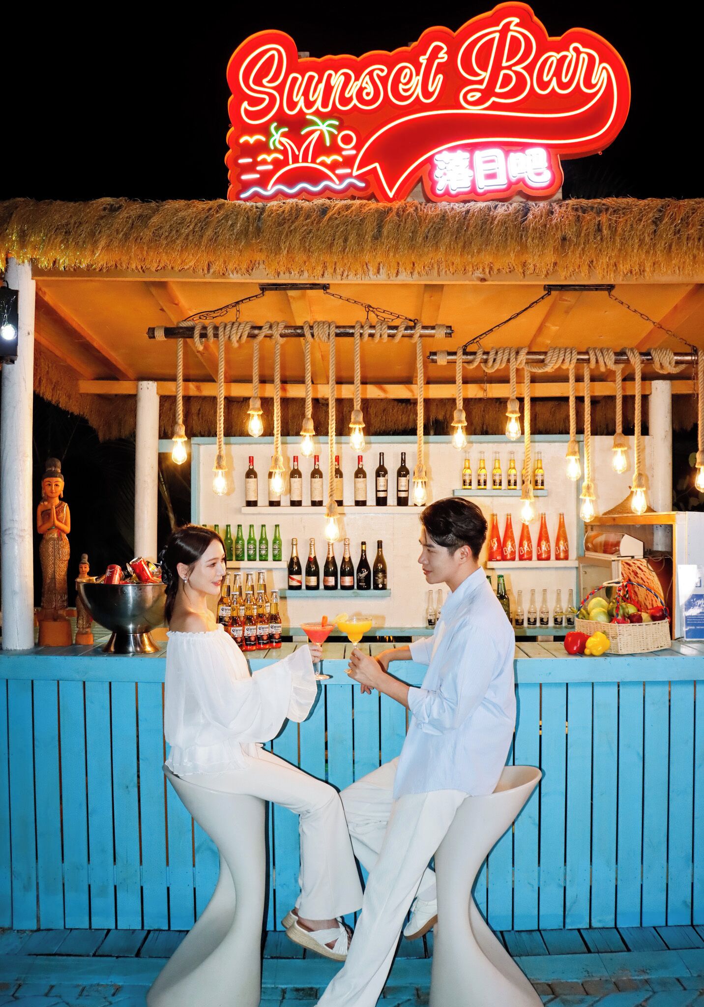 A bar with a neon sign, bottles of alcohol, and a statue.