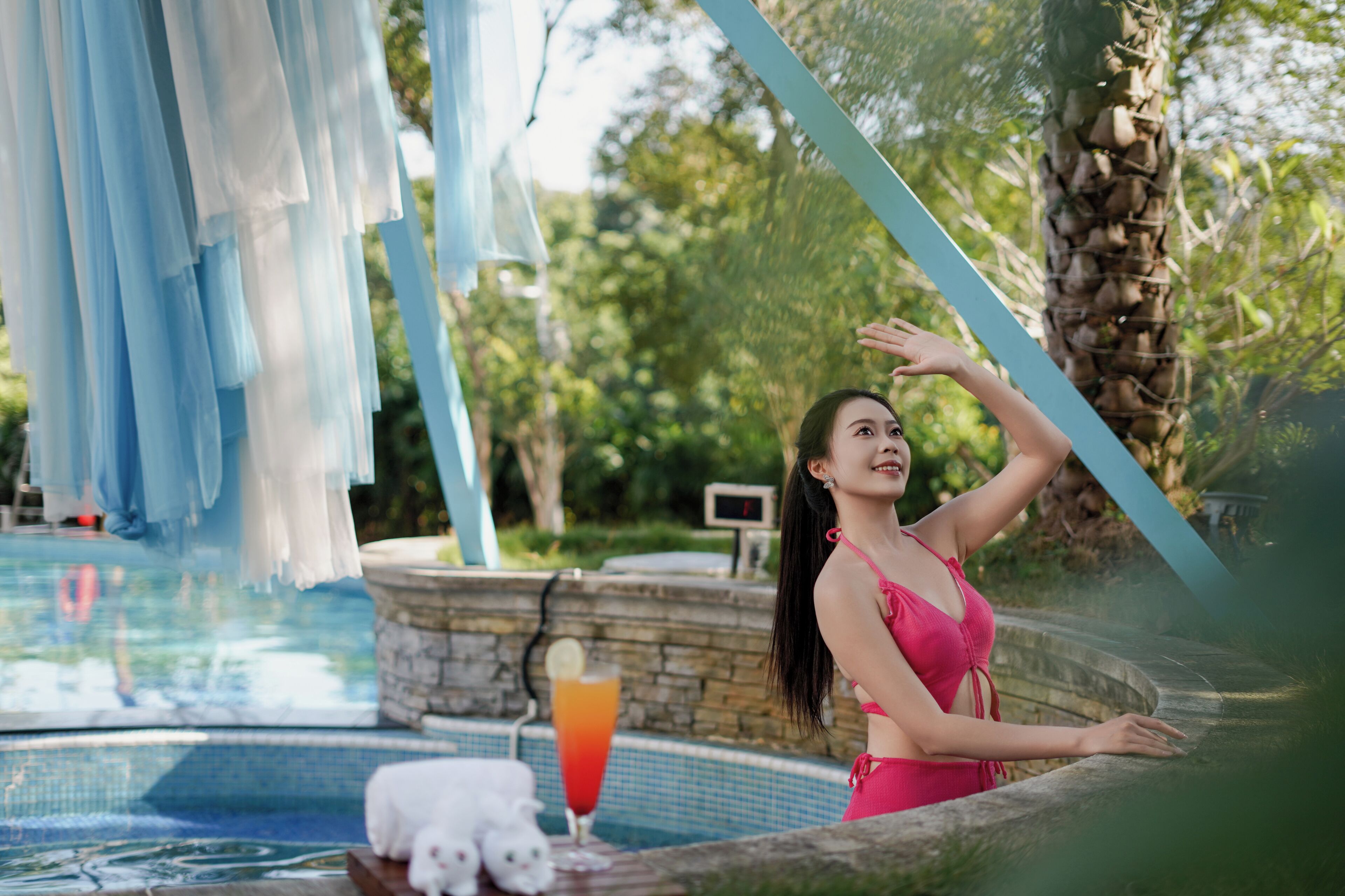 A pool area with a stone wall, a white towel, and a drink on a table.