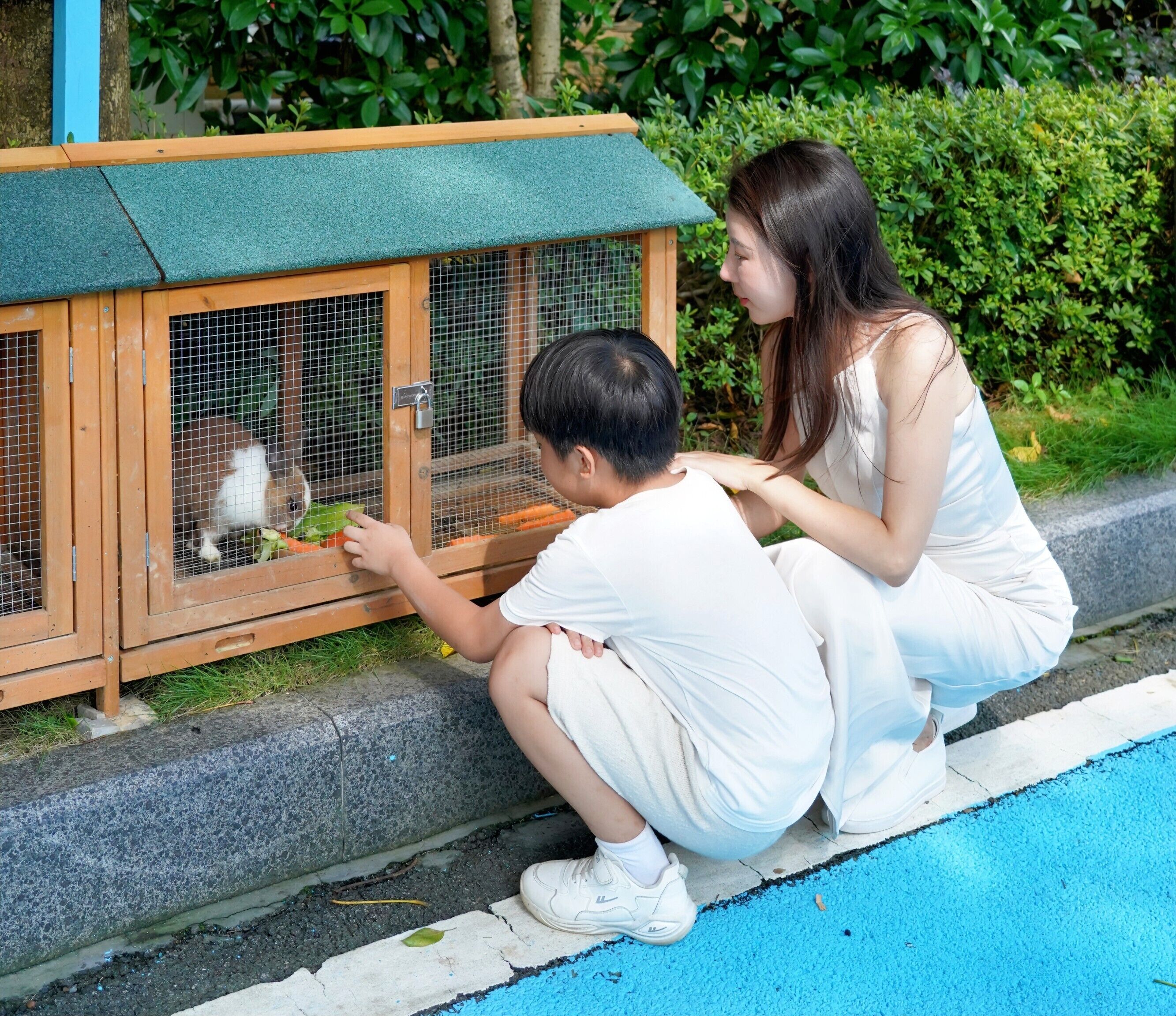 Zwei Personen interagieren mit einem Gehege für Tiere aus Holz.