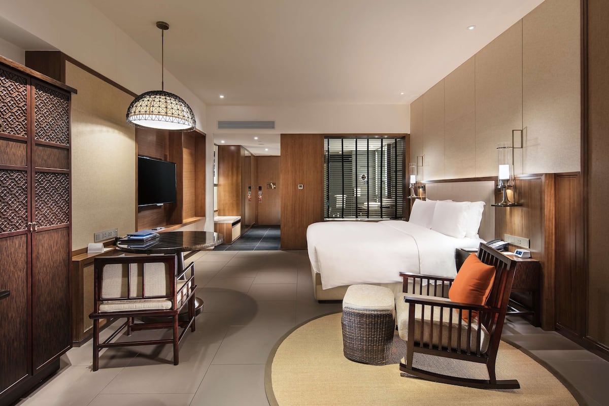 Une chambre d’hôtel avec un grand lit, un bureau avec une chaise, une télévision et une salle de bain visible à travers une porte coulissante.