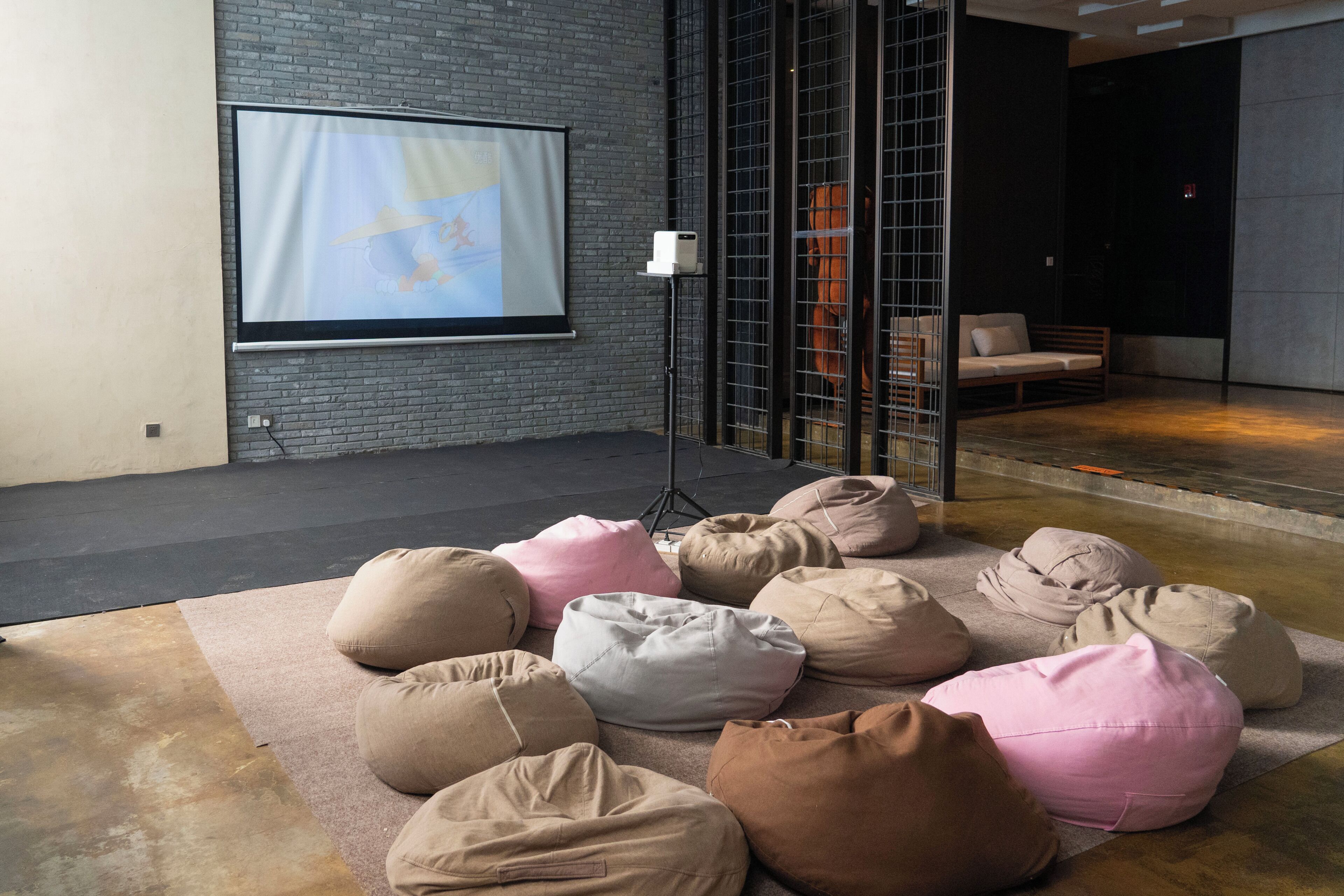 A room with a projector screen, bean bags, a sofa, and a glass partition.