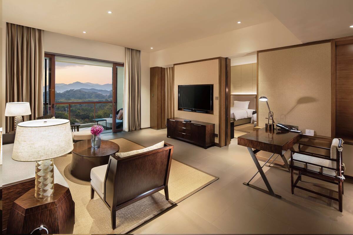 Une chambre d’hôtel dotée d’une grande télévision, d’un bureau, d’une chaise, d’un canapé et offrant une vue sur les montagnes.