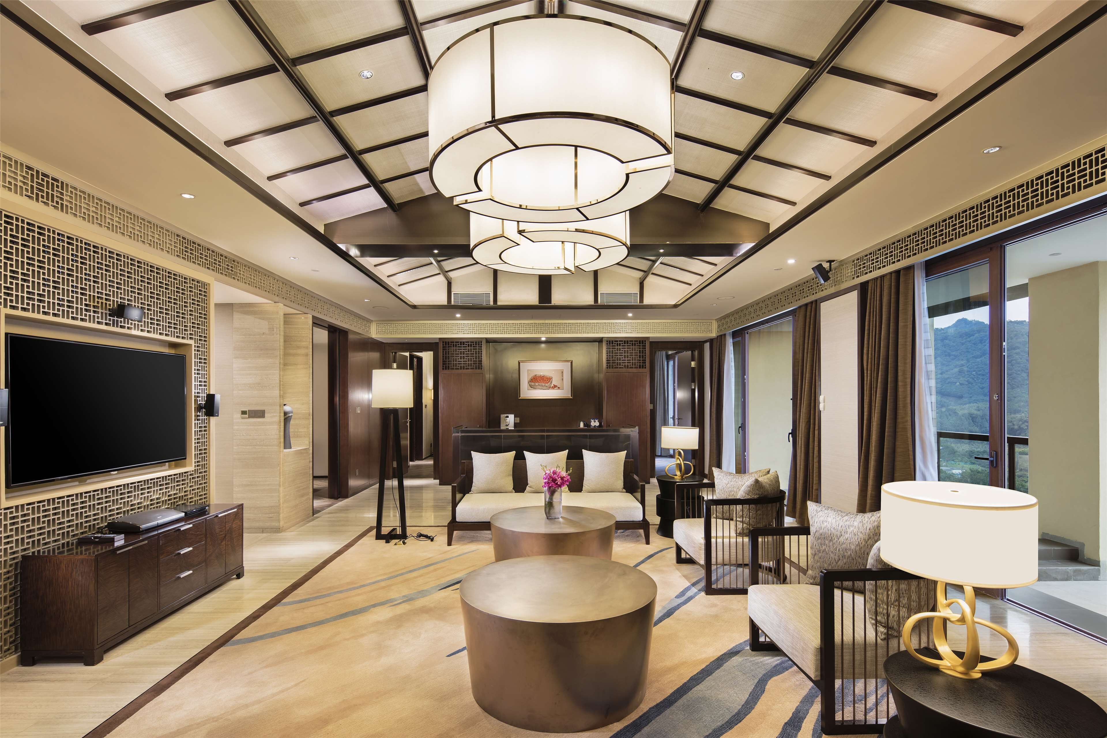 A spacious hotel lobby with a large flat-screen TV, a sofa, a coffee table, and a chandelier.