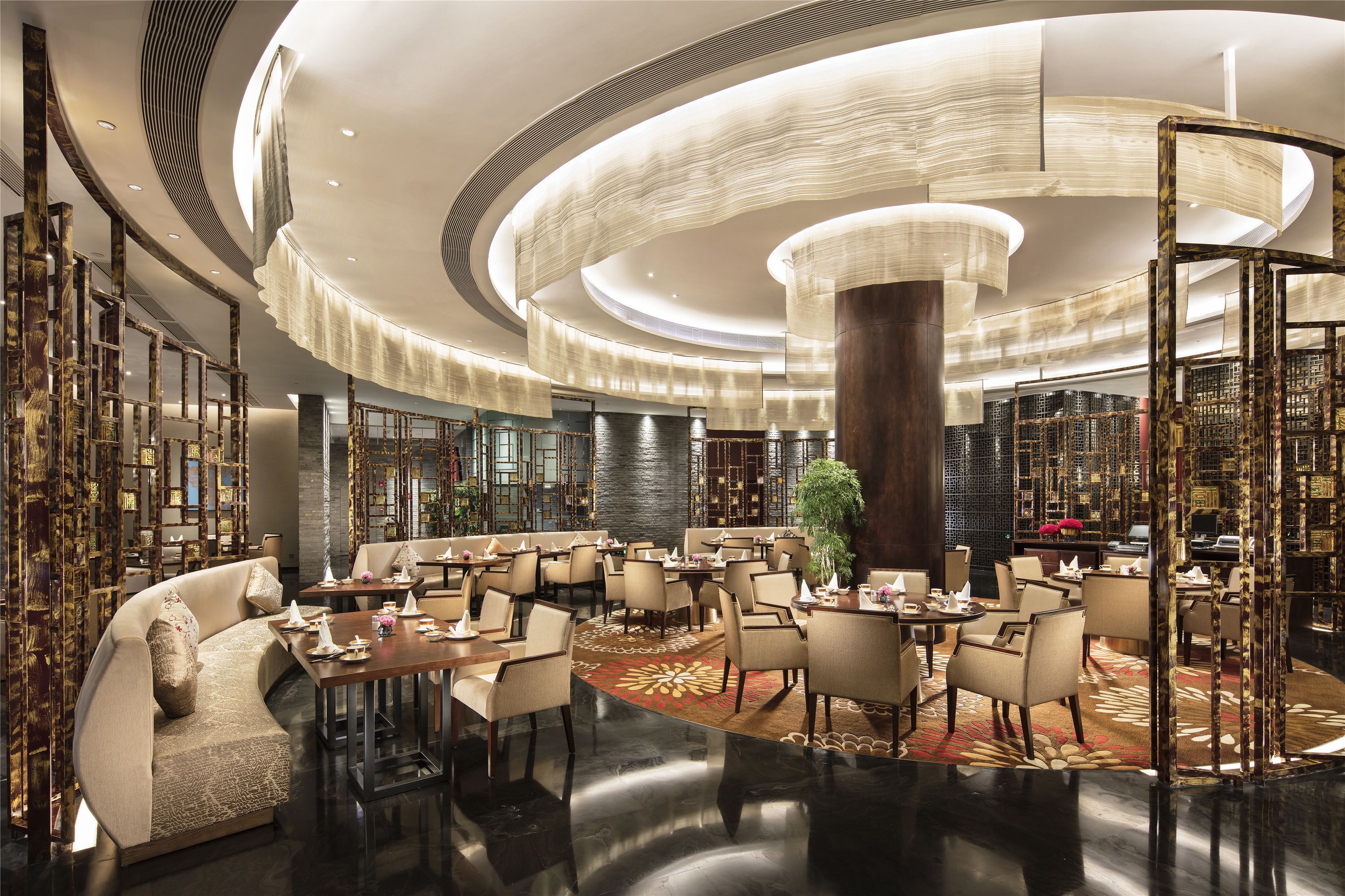 A spacious hotel lobby with a central column, multiple seating areas, and a large chandelier.
