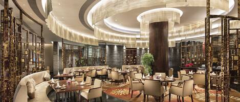A spacious hotel lobby with a central column, multiple seating areas, and a large chandelier.