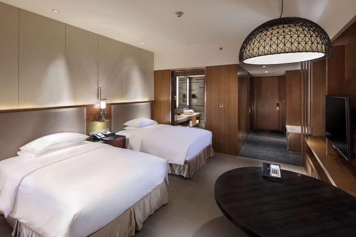 Une chambre d’hôtel avec deux lits, un bureau, une télévision et un lustre moderne.