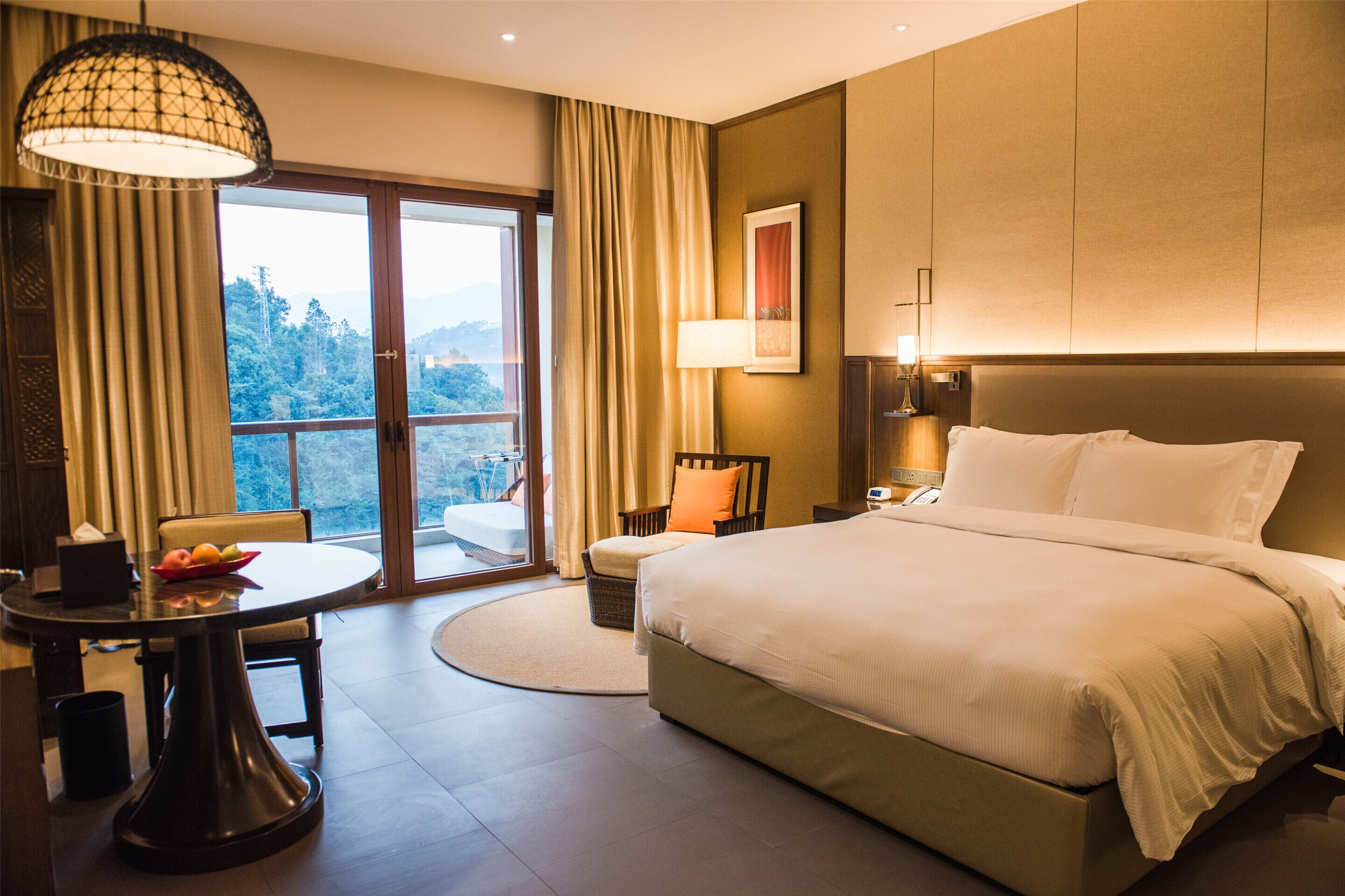 A hotel room with a large bed, a dining table, a chair, a lamp, and a view of the outdoors.