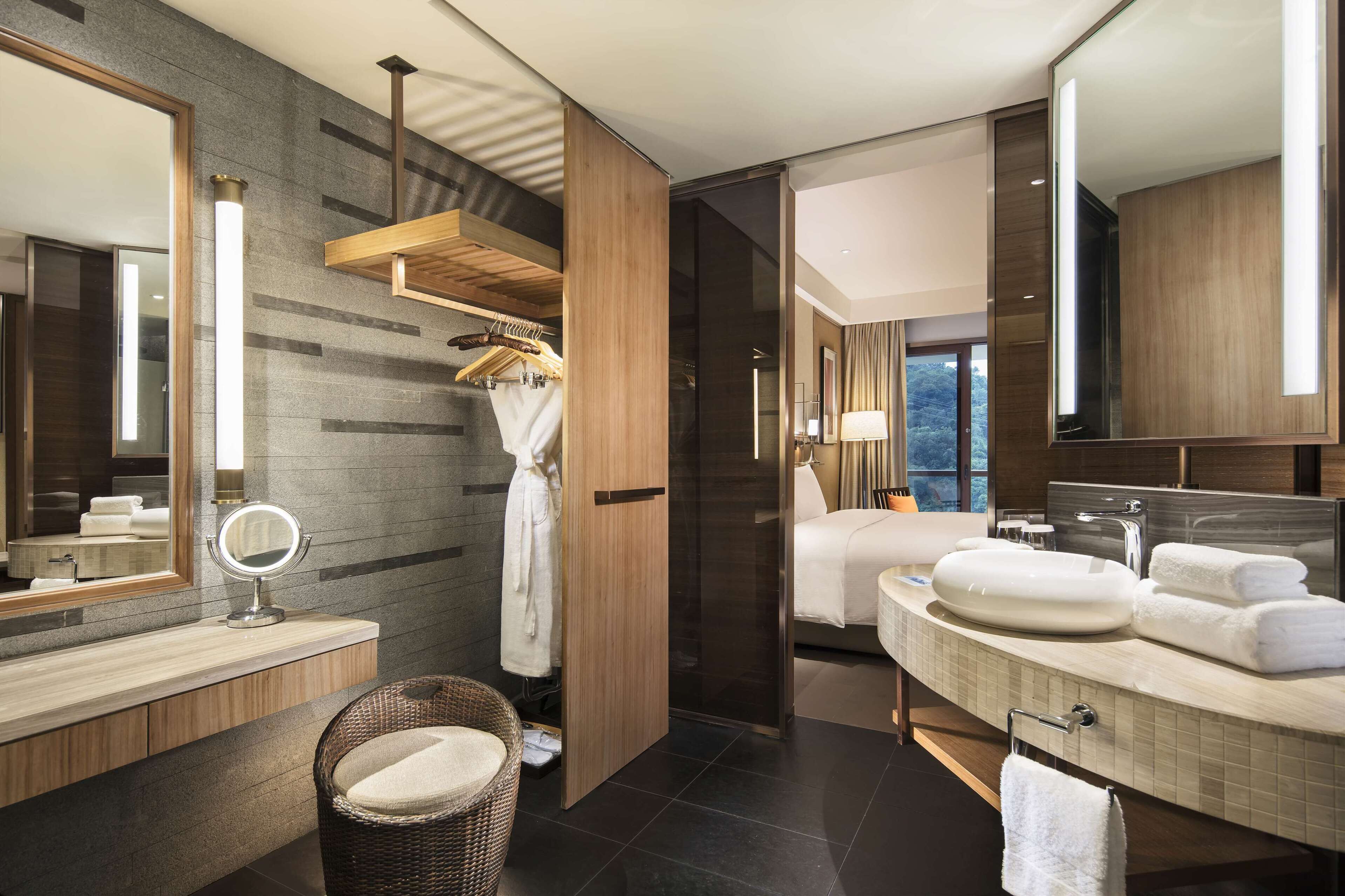 A modern bathroom with a large mirror, two sinks, a robe rack, and a wicker chair.