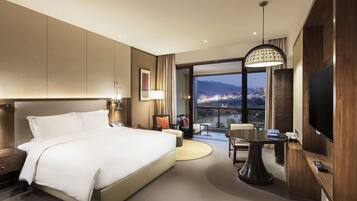 Una habitación de hotel moderna con una cama grande, una mesa de comedor, un televisor y un balcón con vistas a la ciudad.