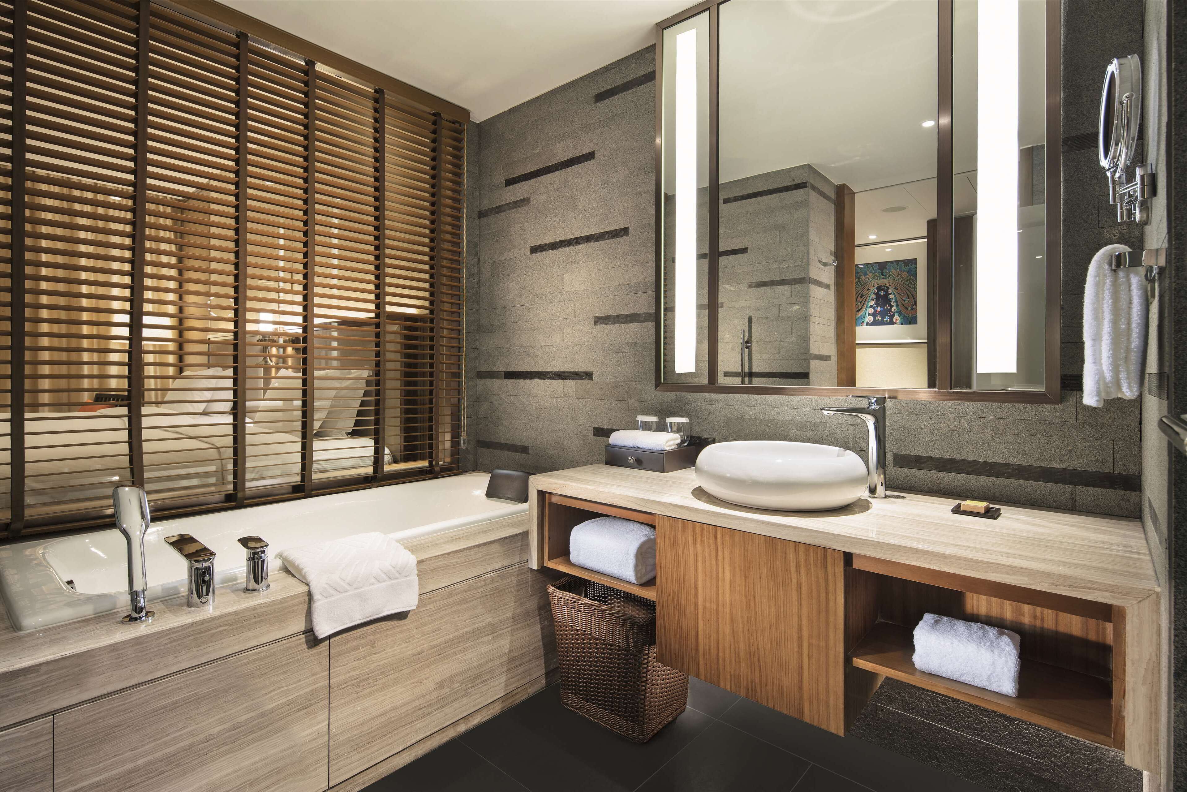 A modern bathroom with a large bathtub, a vanity with a sink, and a mirror. There is a wicker basket under the sink and a towel rack on the wall.