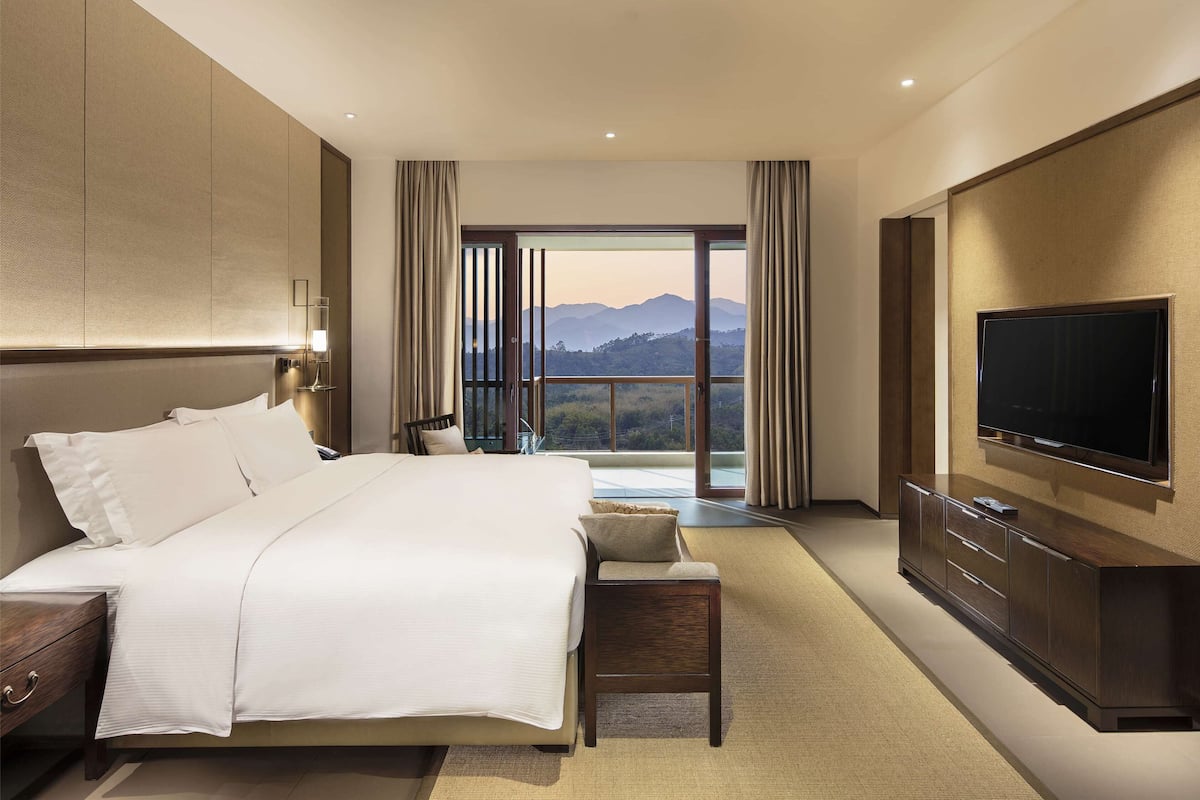 Une chambre d’hôtel avec un grand lit, une télévision, un bureau et une vue sur les montagnes par la fenêtre.