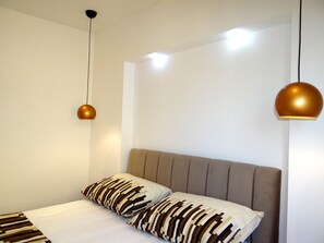 Une chambre à coucher moderne avec un lit, deux lampes suspendues et un mur uni.