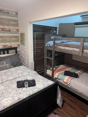 A room with a bunk bed, a desk with a chair, a wardrobe, and a bed with a patterned bedspread.