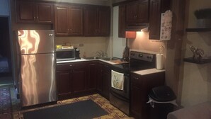 Una cocina compacta con armarios de madera oscura, un refrigerador de acero inoxidable, un microondas, un horno y un lavaplatos.