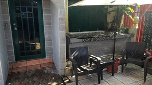 Un patio con puerta verde, piso de baldosas y mobiliario exterior.