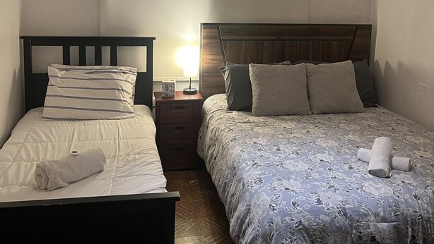 Un dormitorio con dos camas, una mesita de noche con lámpara, aire acondicionado e iluminación colgante original.