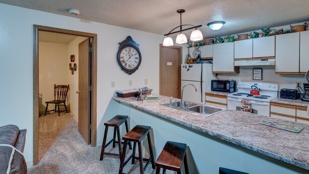 A kitchen with a granite countertop, a sink, a stove, and a microwave. There are three wooden stools and a clock on the wall. - Ski get away 10 minutes to Terry Peak★Deadwood★ Local Brewery across st (Lead)