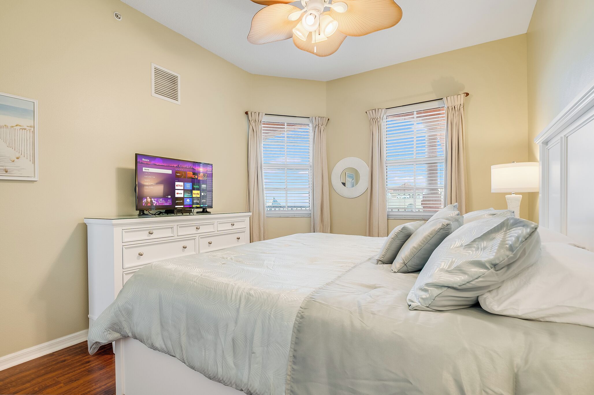 Une chambre à coucher avec un lit, un téléviseur posé sur une commode et deux fenêtres avec des rideaux.