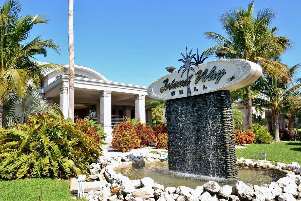 Une enseigne indiquant « Island Grill », avec une fontaine devant, entourée de palmiers et d’un bâtiment doté de colonnes.