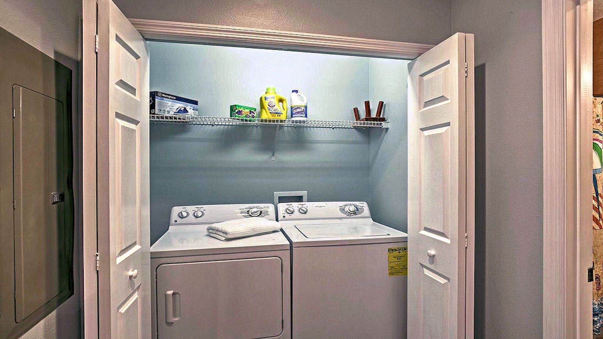 A compact laundry room with a washing machine and dryer, a shelf with cleaning supplies, and a door with a handle.