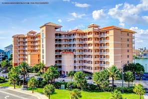 A multi-story hotel with balconies, a marina in the background, and palm trees in the foreground.