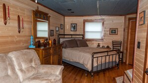 A cozy log cabin bedroom with a bed, a sofa, a dresser, and a window with blinds. - On the Wine Trail - Shawnee & Giant City Minutes Away- Jetted Tubs (Makanda)