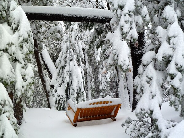 Um banco de madeira coberto de neve, rodeado por árvores carregadas de neve.