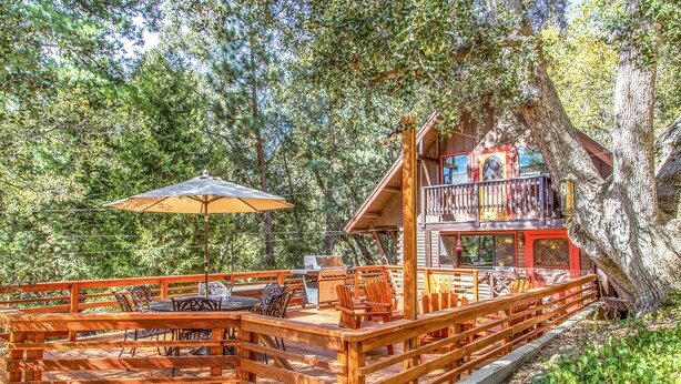 A wooden deck with outdoor furniture, a large umbrella, and a cabin with a balcony.