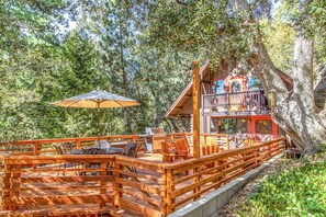 A wooden deck with outdoor furniture, a large umbrella, and a cabin with a balcony.