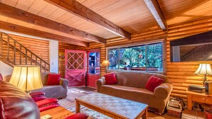 A log cabin interior with a wooden ceiling, a red door, a sofa, a coffee table, and a lamp.