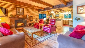 A cozy log cabin interior with a fireplace, leather chairs, and a dining area.