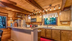 A log cabin-style kitchen with wooden cabinets, a central island, a microwave, and a window with a view of trees.