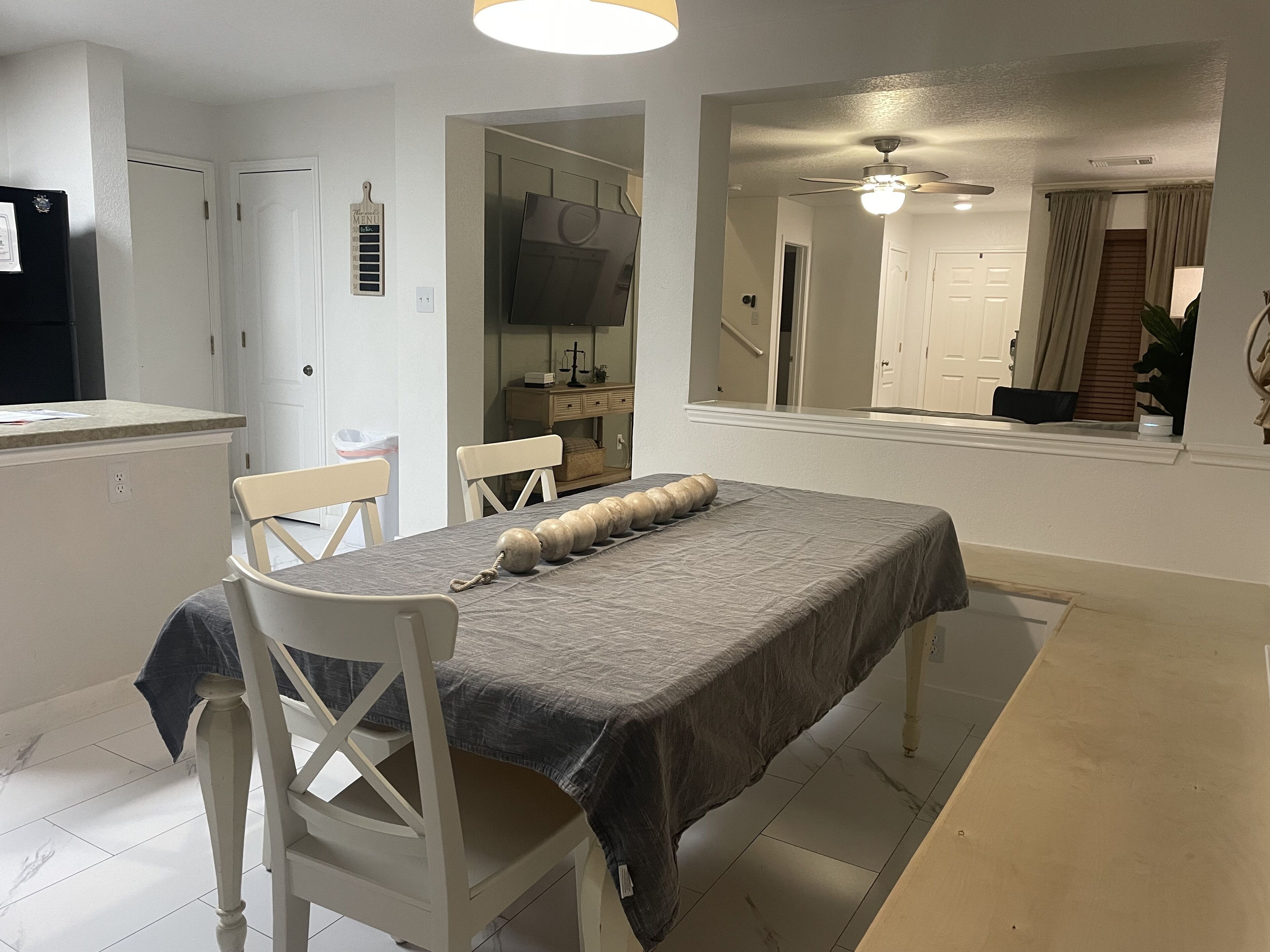 A dining area with a table set for two, a ceiling fan, and a view of a hallway.