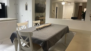 A dining area with a table set for two, a ceiling fan, and a view of a hallway.