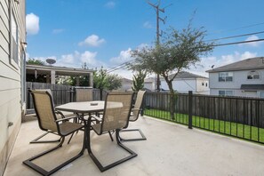 Un patio con una mesa y sillas, un cerco de madera y vistas a casas vecinas.
