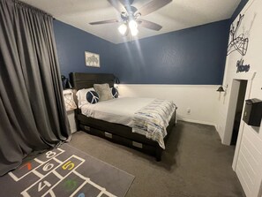 Un dormitorio con cama, mesita de noche, ventilador de techo, lámpara de pared y una puerta con placa.