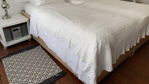A neatly made bed with a white duvet and pillows, a bedside table with a lamp, and a patterned rug on the floor. - Agapi Nefeli, unique roofterrace view to sea port & town island MamaMia Skopelos (Skopelos)