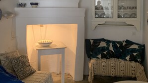 A cozy living room with a fireplace, a sofa, a table with a bowl, and a cabinet with dishes. - Agapi Nefeli, unique roofterrace view to sea port & town island MamaMia Skopelos (Skopelos)