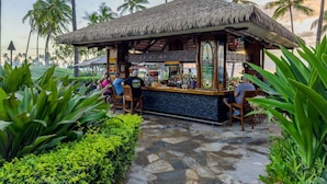 Eine Strandbar mit Reetdach, umgeben von üppiger Vegetation und Palmen.