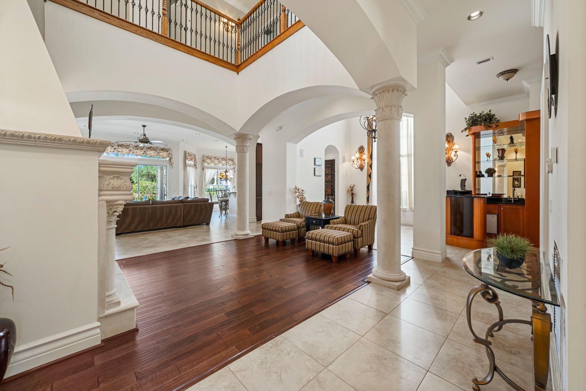 A spacious living area with a high ceiling, wooden flooring, and a central seating area with ottomans and a sofa.
