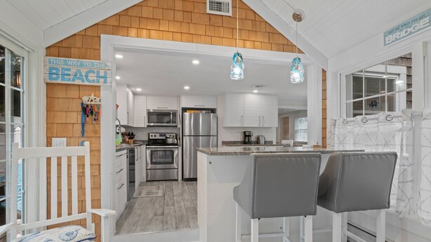 A modern kitchen with white cabinets, stainless steel appliances, and a wooden accent wall. There is a bar area with two bar stools and a bench.