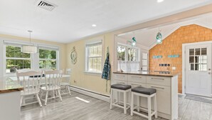A kitchen with a wooden island, white cabinets, and a dining area with white chairs.