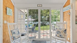 A covered patio with white rocking chairs and a view of the backyard.