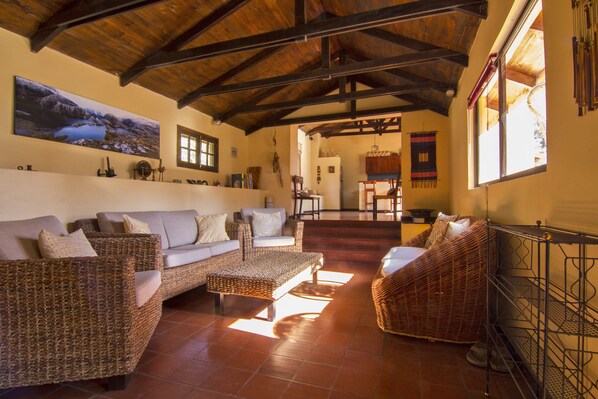 A spacious living area with wicker furniture, a large painting on the wall, and a view of the kitchen through an open doorway.