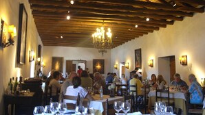 Un restaurante con vigas de madera en el techo, mesas dispuestas con copas de vino y platos, y comensales cenando.